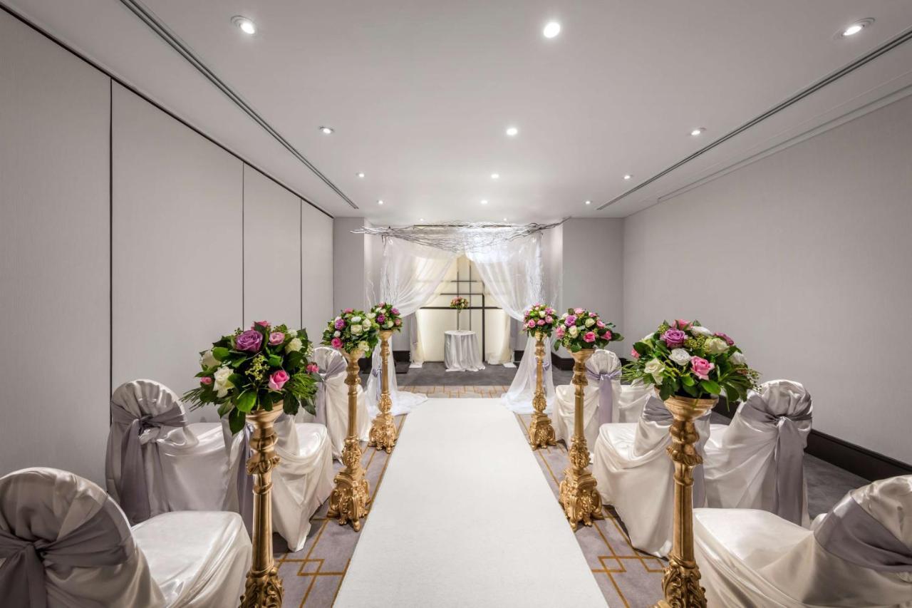 Radisson Blu Plaza Hotel Σίδνεϊ Εξωτερικό φωτογραφία The photo shows a beautifully arranged indoor event space, likely set up for a wedding ceremony. There is a long white aisle runner leading to a decorated archway at the end. On either side of the aisle, there are elegant chairs draped in white fabri