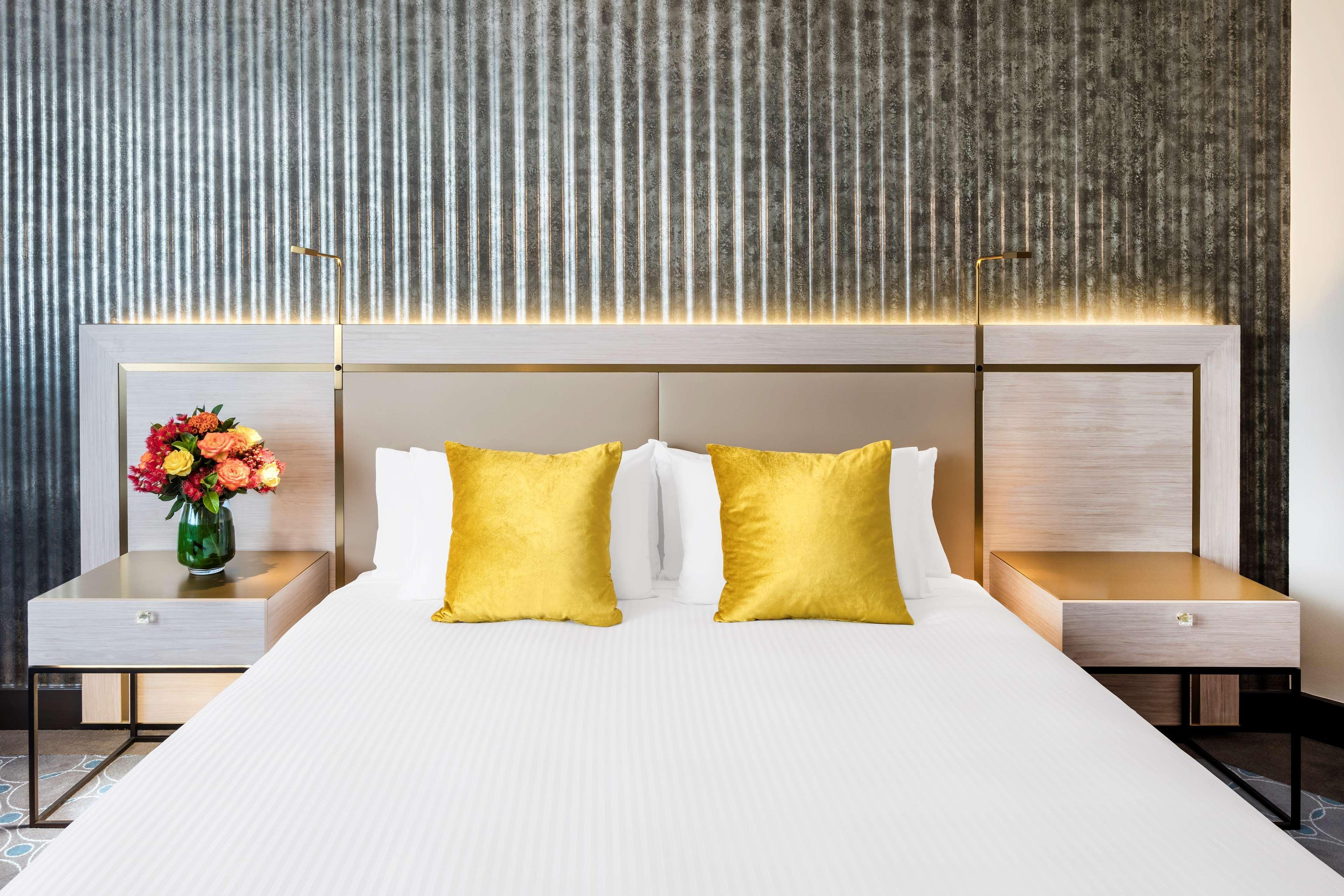 Radisson Blu Plaza Hotel Σίδνεϊ Εξωτερικό φωτογραφία The photo shows a stylish hotel room with a modern design. In the center, there's a neatly made bed with a white bedspread and two decorative yellow pillows. The headboard has a sleek, contemporary look, and there are two bedside tables on either sid