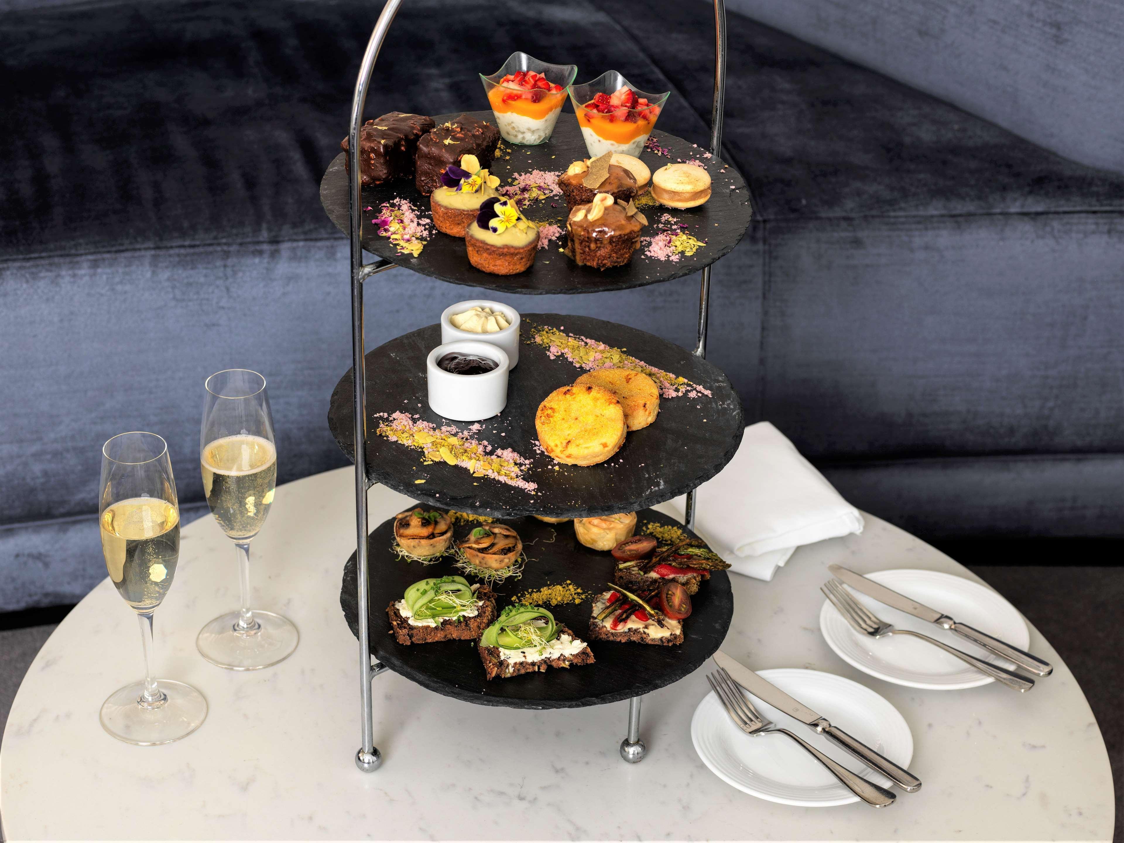 Radisson Blu Plaza Hotel Σίδνεϊ Εξωτερικό φωτογραφία The photo depicts a tiered serving stand filled with various desserts and snacks. The stand has three levels:

1. **Top Tier**: Features a selection of small desserts, including colorful cups of fruit, cakes, and pastries.
   
2. **Middle Tier**: Con