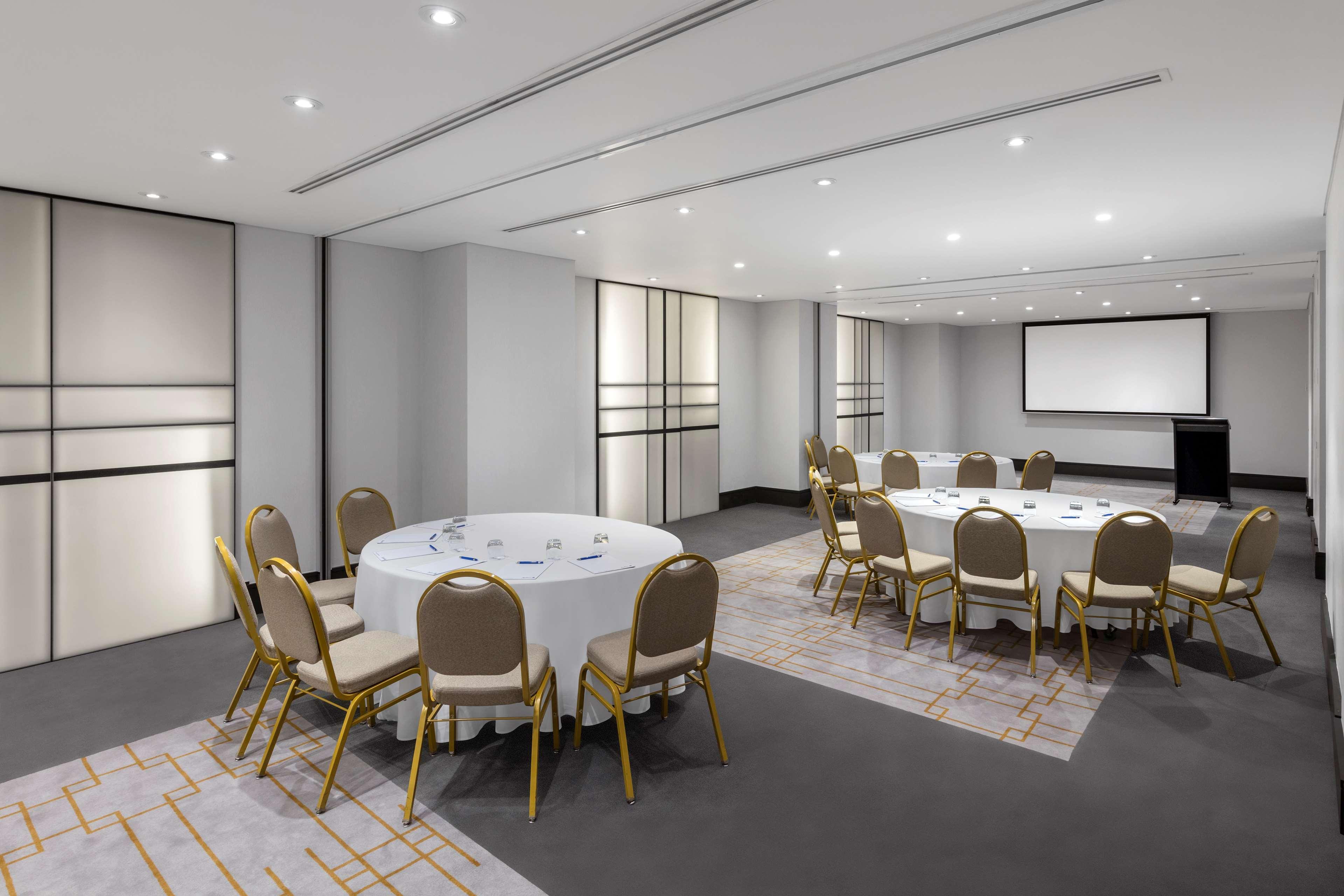 Radisson Blu Plaza Hotel Σίδνεϊ Εξωτερικό φωτογραφία The photo shows a modern meeting room or conference space. It features several round tables covered with white tablecloths, surrounded by gold-colored chairs. The walls are light-colored, and there are large, sliding partitions that could separate th
