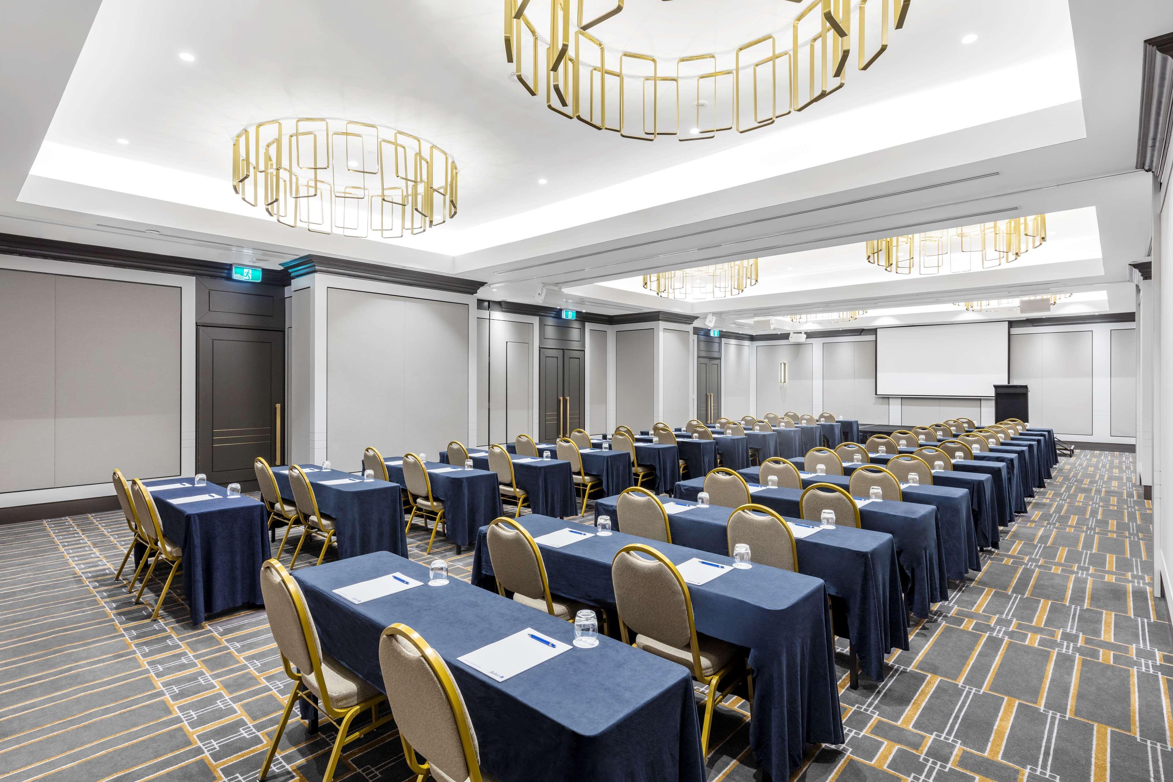 Radisson Blu Plaza Hotel Σίδνεϊ Εξωτερικό φωτογραφία The photo shows a conference room set up for a meeting or seminar. The room features rows of tables covered with dark blue tablecloths and gold-accented chairs. Each table has a piece of paper and a glass of water placed on it. The lighting is modern