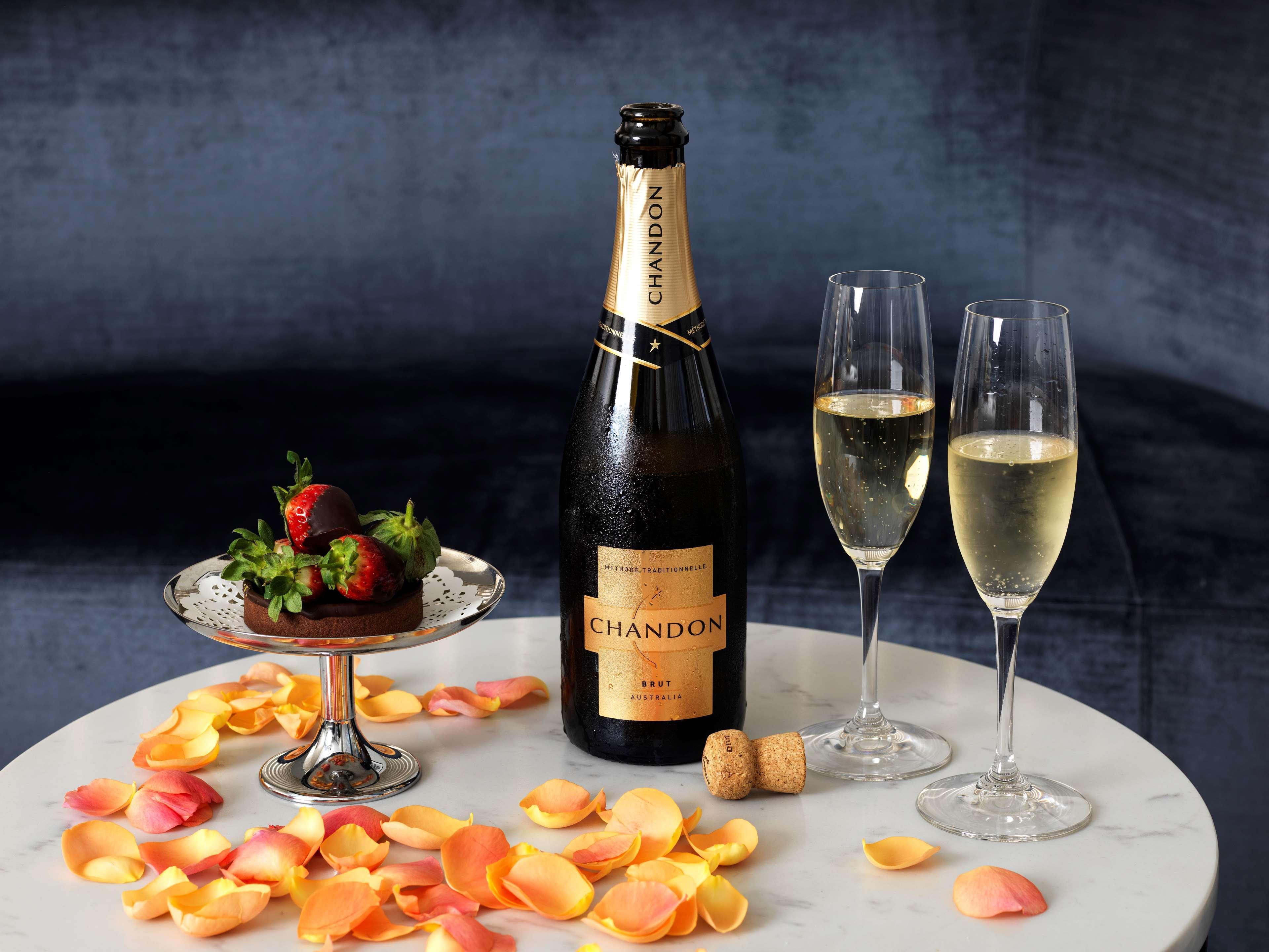 Radisson Blu Plaza Hotel Σίδνεϊ Εξωτερικό φωτογραφία The image shows a stylish setting featuring a bottle of Chandon sparkling wine accompanied by two filled champagne flutes. There is a silver plate with a dessert topped with strawberries and some scattered flower petals on the table, creating a roman