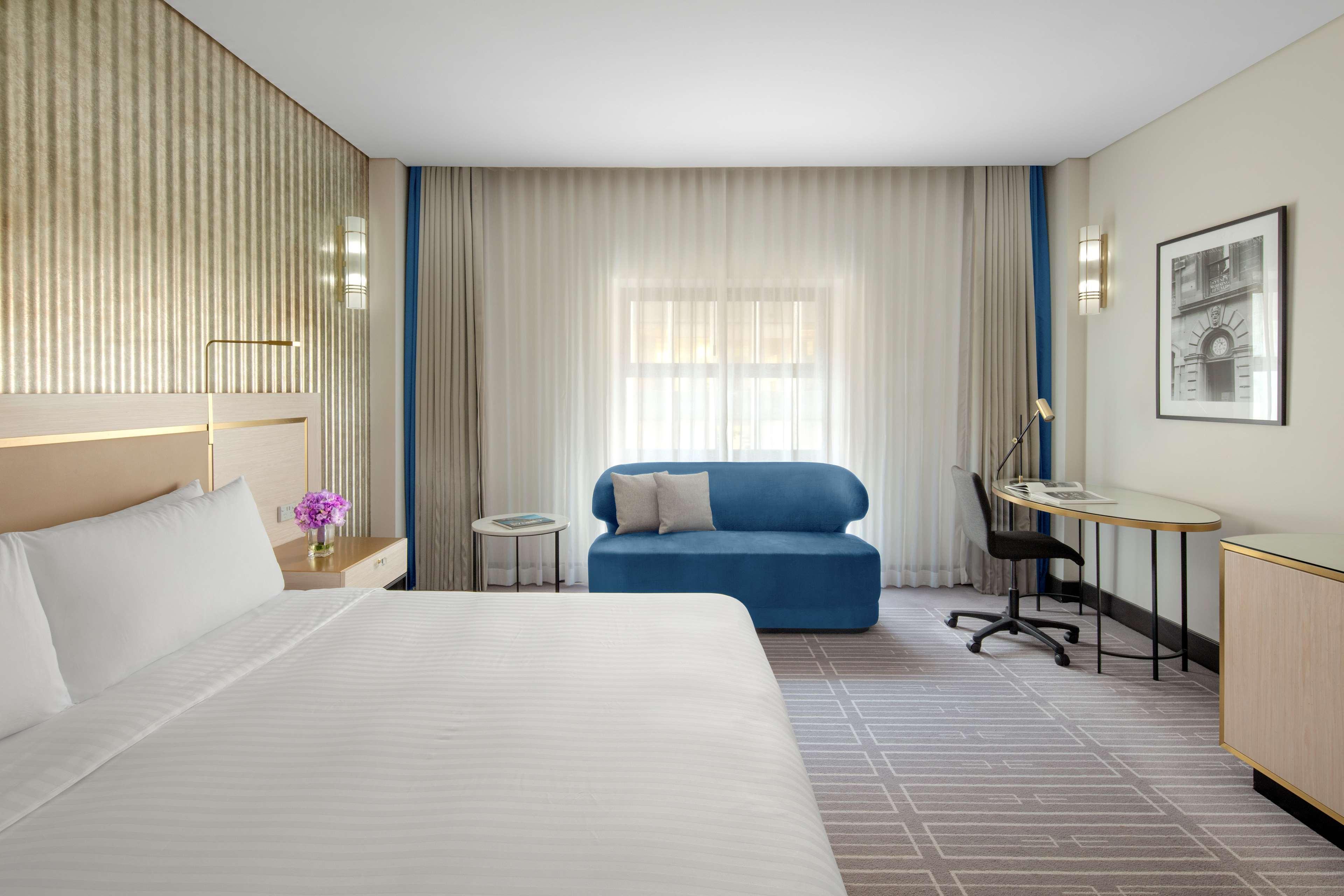 Radisson Blu Plaza Hotel Σίδνεϊ Εξωτερικό φωτογραφία The photo shows a modern hotel room featuring a large bed with white linens. There's a small table with a flower vase next to the bed. A blue sofa is positioned against one wall, and a desk with a chair is situated nearby. The room has soft, diffused
