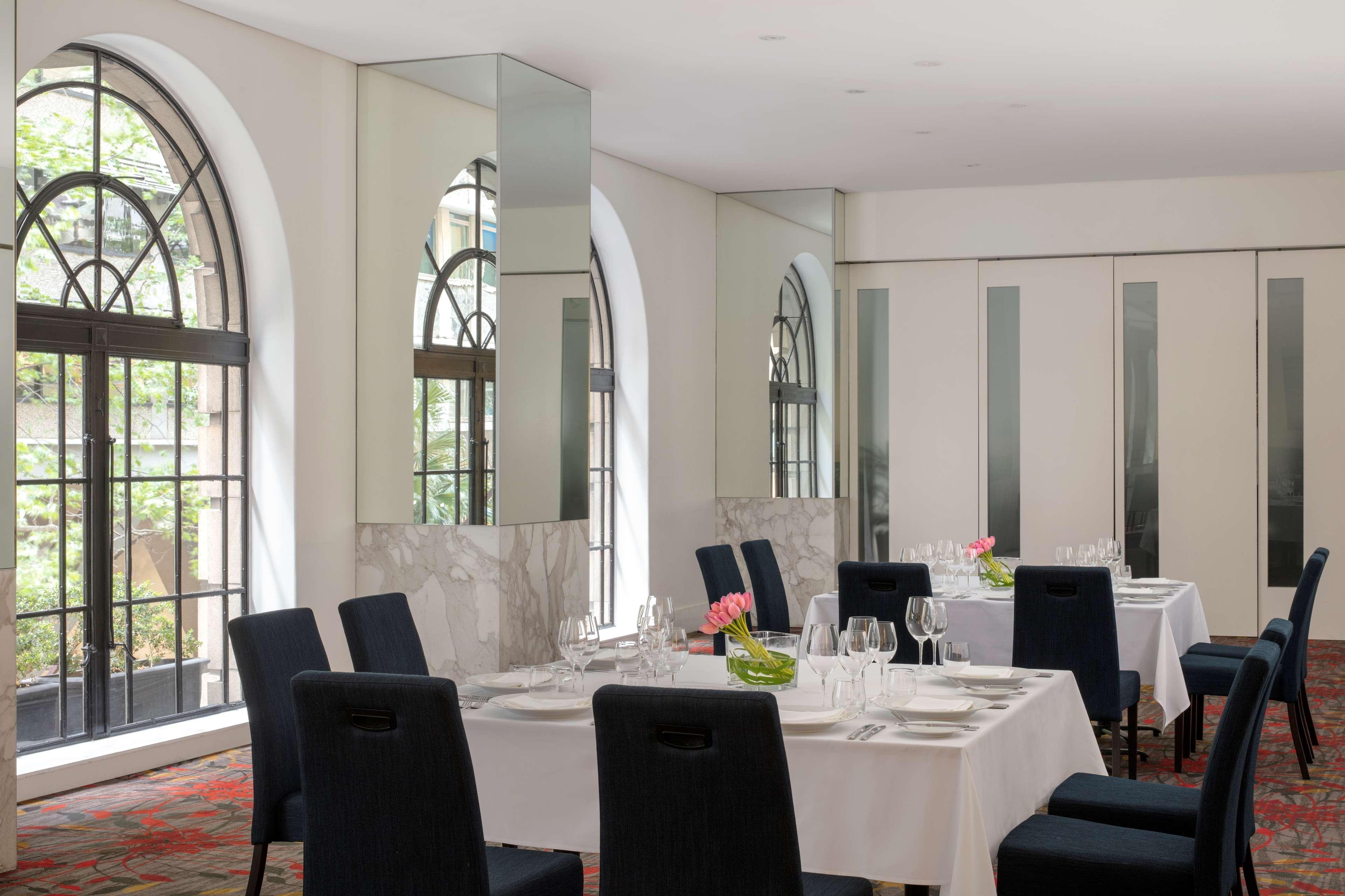 Radisson Blu Plaza Hotel Σίδνεϊ Εξωτερικό φωτογραφία The photo shows a dining area in a restaurant or hotel. It features elegant décor with large arched windows that allow natural light to enter. The walls are light-colored, and there are mirrors that reflect the space, creating a more open and bright 