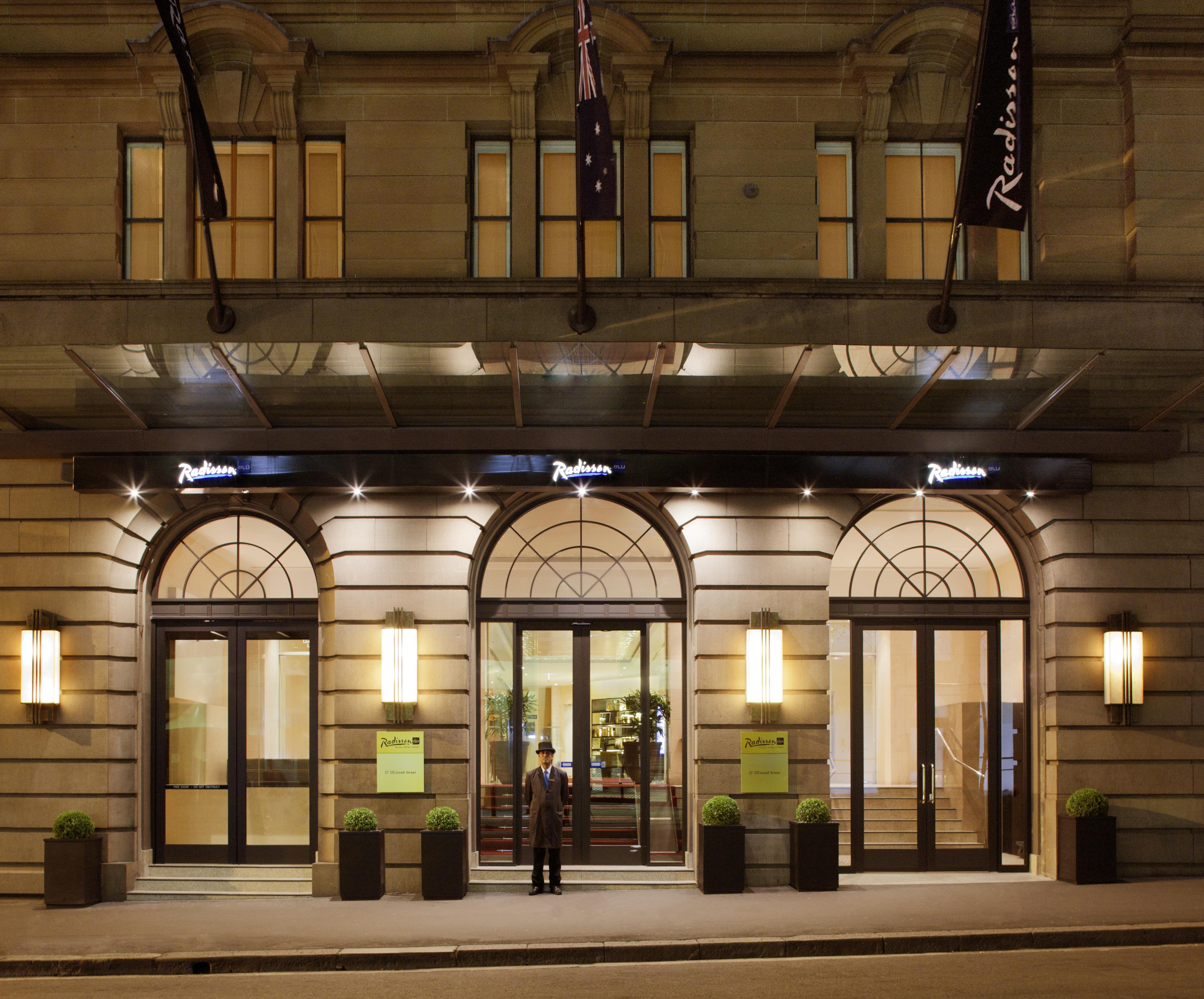 Radisson Blu Plaza Hotel Σίδνεϊ Εξωτερικό φωτογραφία The photo depicts the entrance of a Radisson hotel. The building features elegant architecture, with large arched windows and a well-lit canopy above the entrance. There are two potted plants on either side of the doors, which are framed by modern li