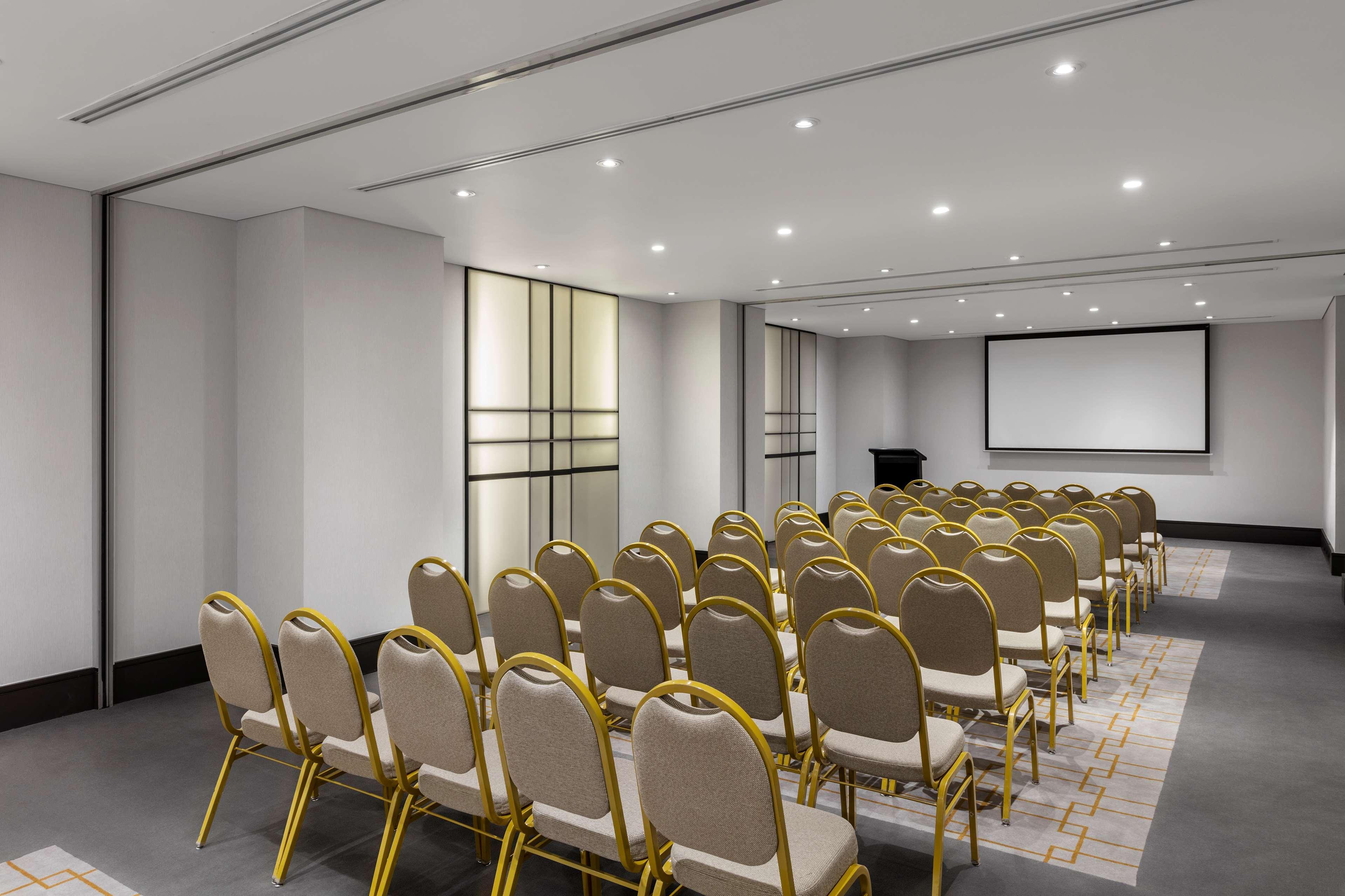 Radisson Blu Plaza Hotel Σίδνεϊ Εξωτερικό φωτογραφία The photo shows a conference room or meeting space. It features a neat arrangement of rows of beige chairs with gold frames facing a projection screen at the front. The room is well-lit with recessed lighting and has a modern design, including a clea