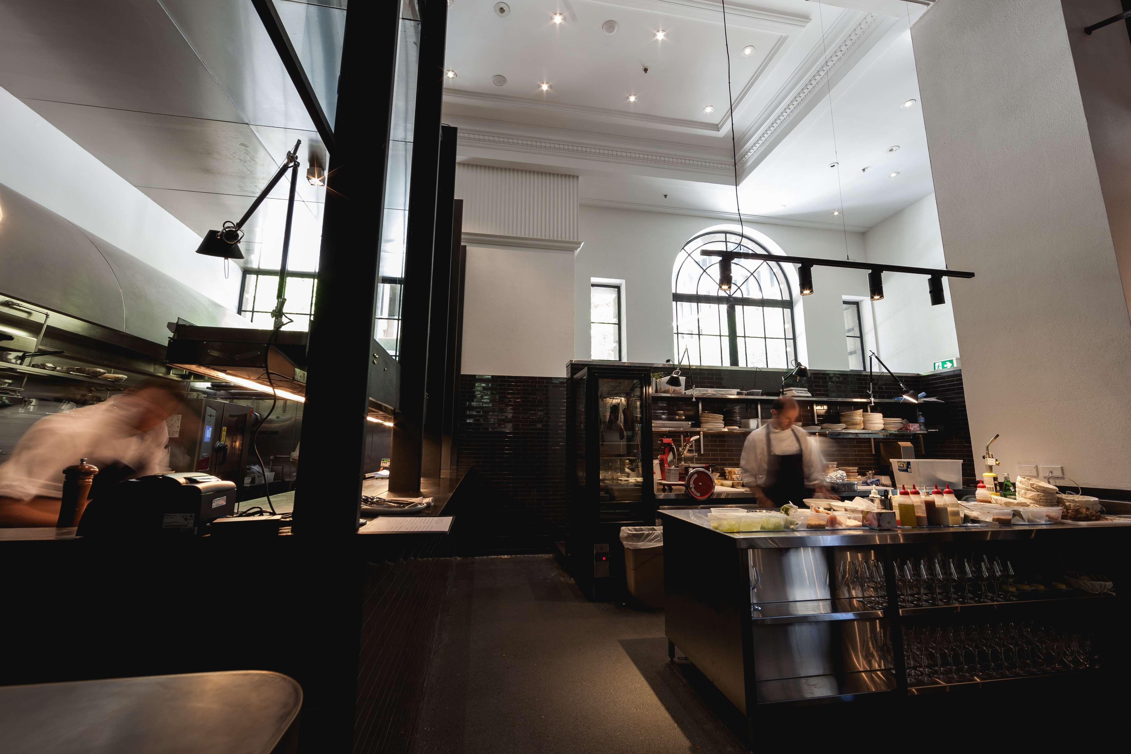 Radisson Blu Plaza Hotel Σίδνεϊ Εξωτερικό φωτογραφία The photo shows a modern kitchen or dining area of a restaurant. The space features high ceilings and large windows, allowing natural light to fill the room. There are sleek black structures, likely part of the kitchen’s infrastructure, along with a 