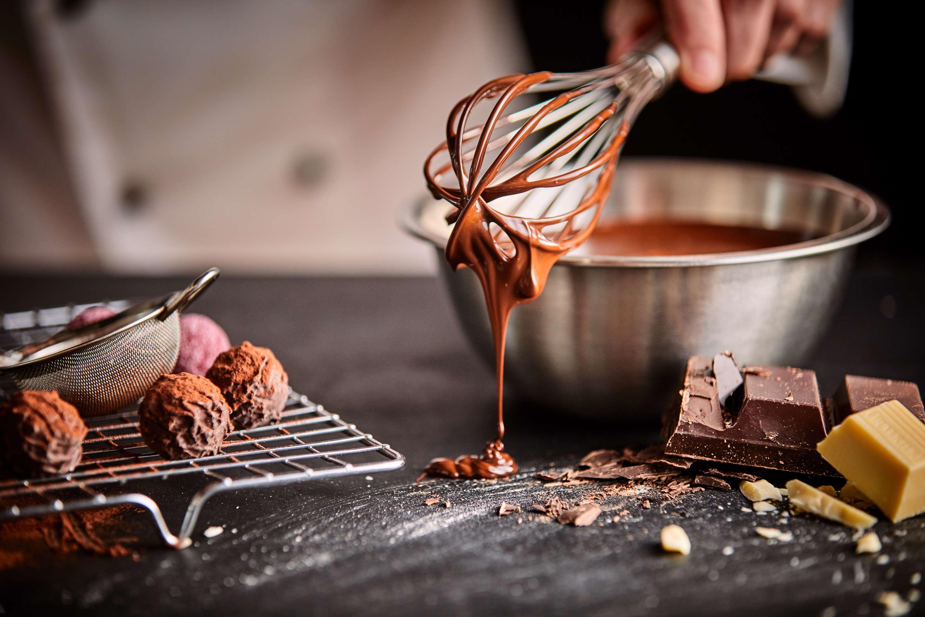Radisson Blu Plaza Hotel Σίδνεϊ Εξωτερικό φωτογραφία The photo shows a scene of chocolate preparation in a kitchen. A hand is holding a whisk, dripping melted chocolate into a mixing bowl. Nearby, there are chocolate truffles arranged on a wire rack, pieces of chocolate scattered on the surface, and a 