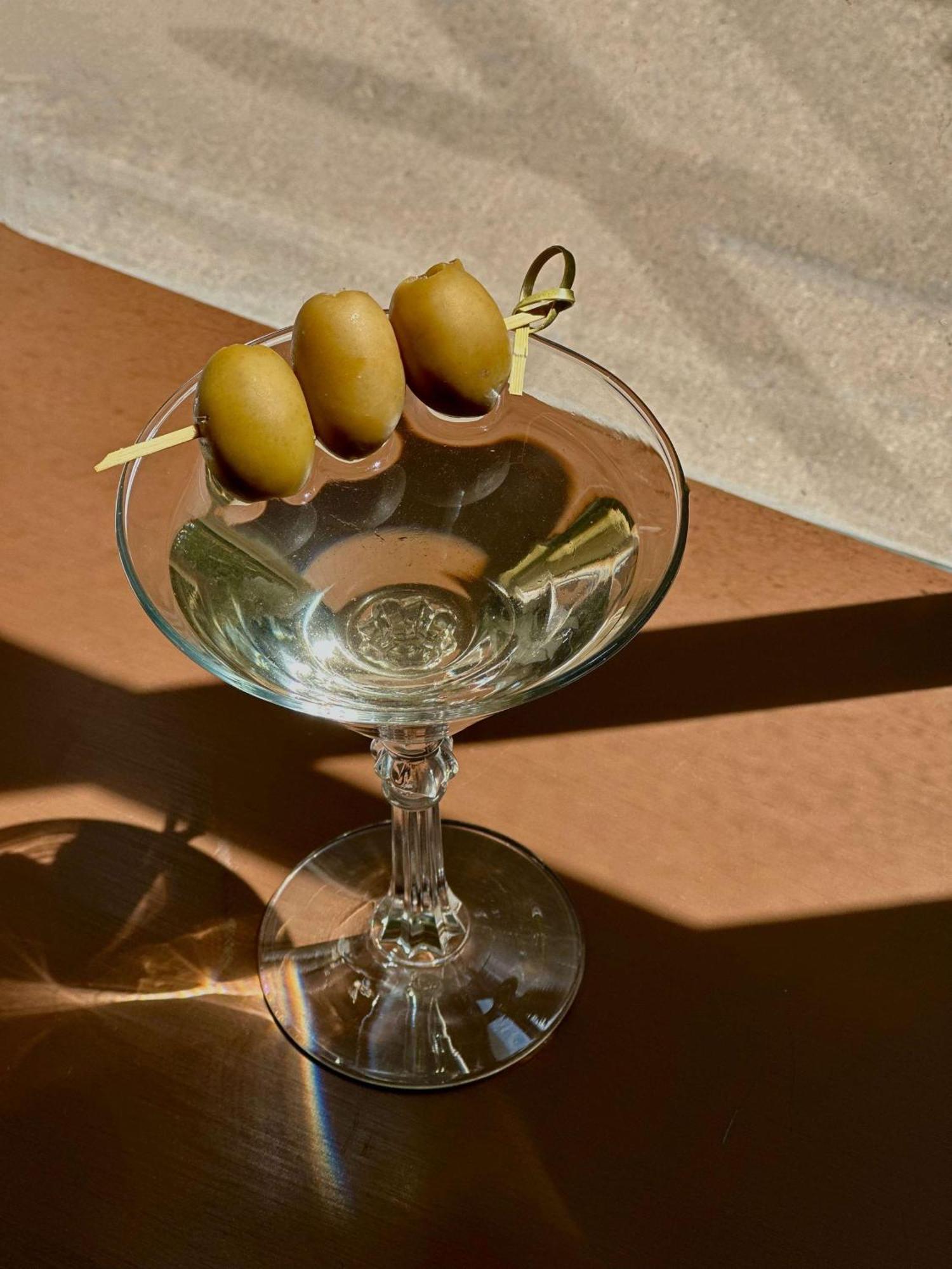 Radisson Blu Plaza Hotel Σίδνεϊ Εξωτερικό φωτογραφία The image shows a clear martini glass with three green olives skewered on a toothpick resting on the rim. The glass is empty, reflecting light and showcasing its elegant shape. The background features a warm-toned surface and possibly a shadow, enhan