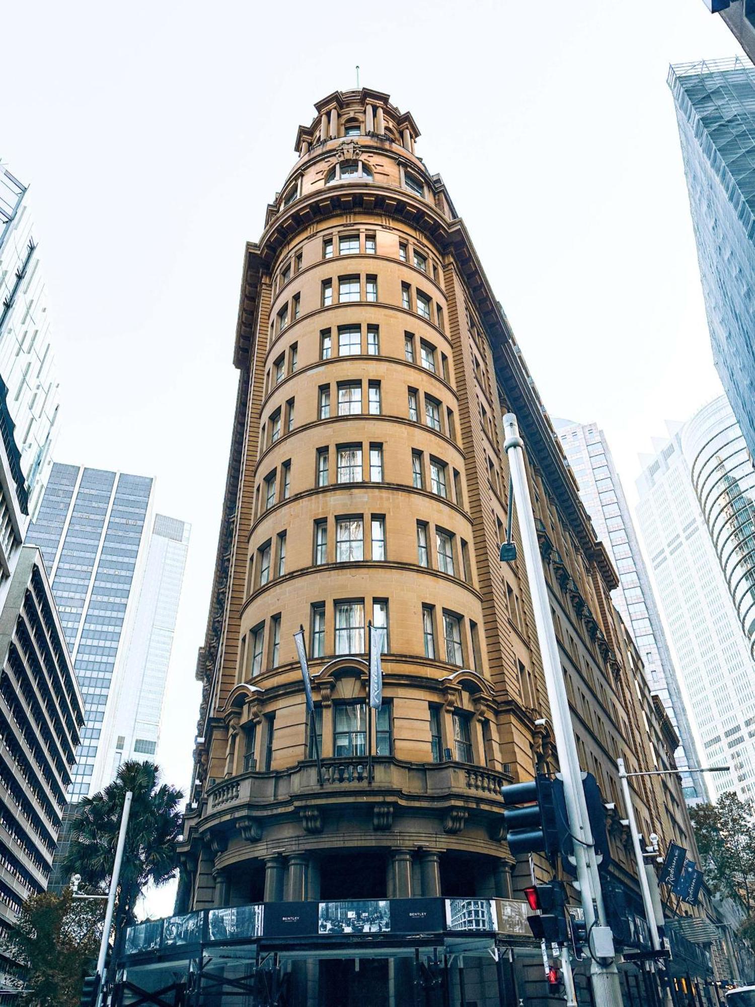 Radisson Blu Plaza Hotel Σίδνεϊ Εξωτερικό φωτογραφία The image shows a distinctive architectural building characterized by its curved facade and a warm, yellowish-brown exterior. The structure appears to have multiple floors, with large windows arranged symmetrically. Surrounding the building are moder