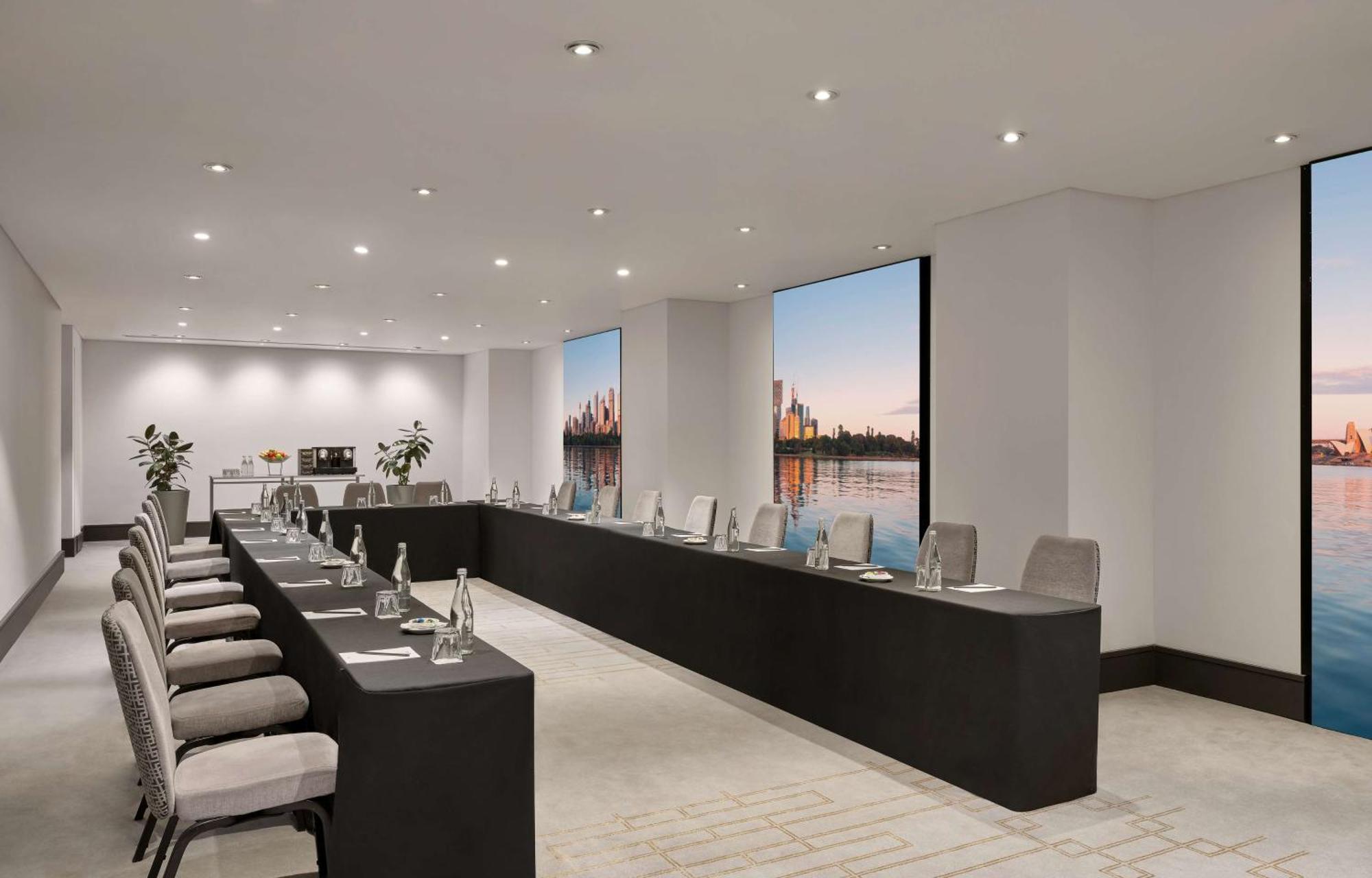 Radisson Blu Plaza Hotel Σίδνεϊ Εξωτερικό φωτογραφία The photo depicts a modern conference room set up for a meeting. The room features a long, rectangular table with multiple chairs arranged along its sides. Each chair is equipped with items such as water bottles and notepads. Large windows allow natu
